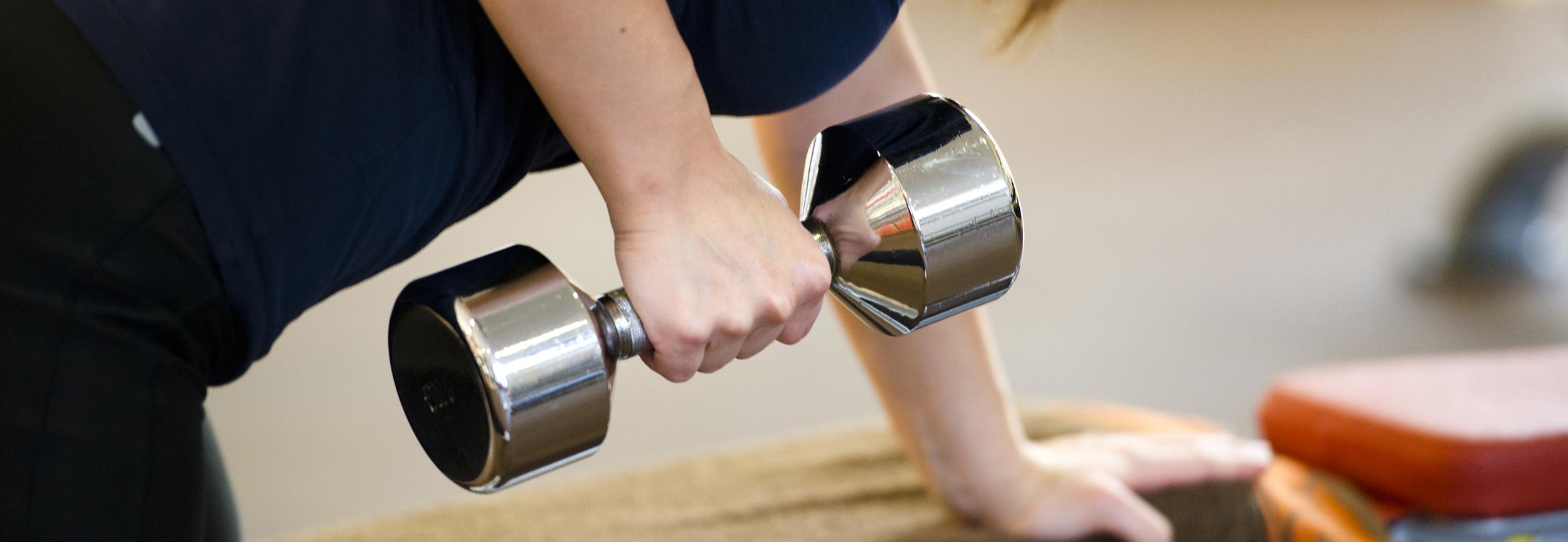 Frau macht eine Bizepsübung mit einer Hantel, während sie auf einer Trainingsbank lehnt.