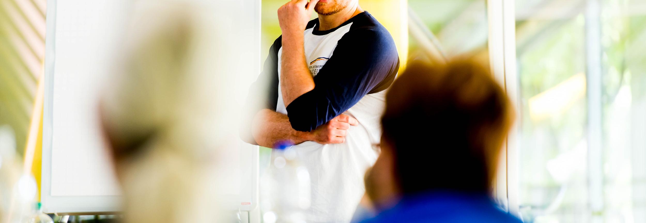 Mann mit Brille spricht vor einer Gruppe, ein Flipchart ist im Hintergrund sichtbar.